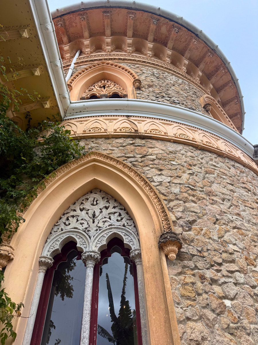 Low-angle close-up of a round, textured stone tower at a palace in Sintra, featuring intricate, carved stone window frames and pink accents.