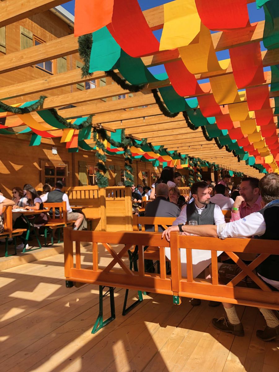 Outdoor Oktoberfest beer garden in Munich with wooden benches and colorful hanging decorations overhead.