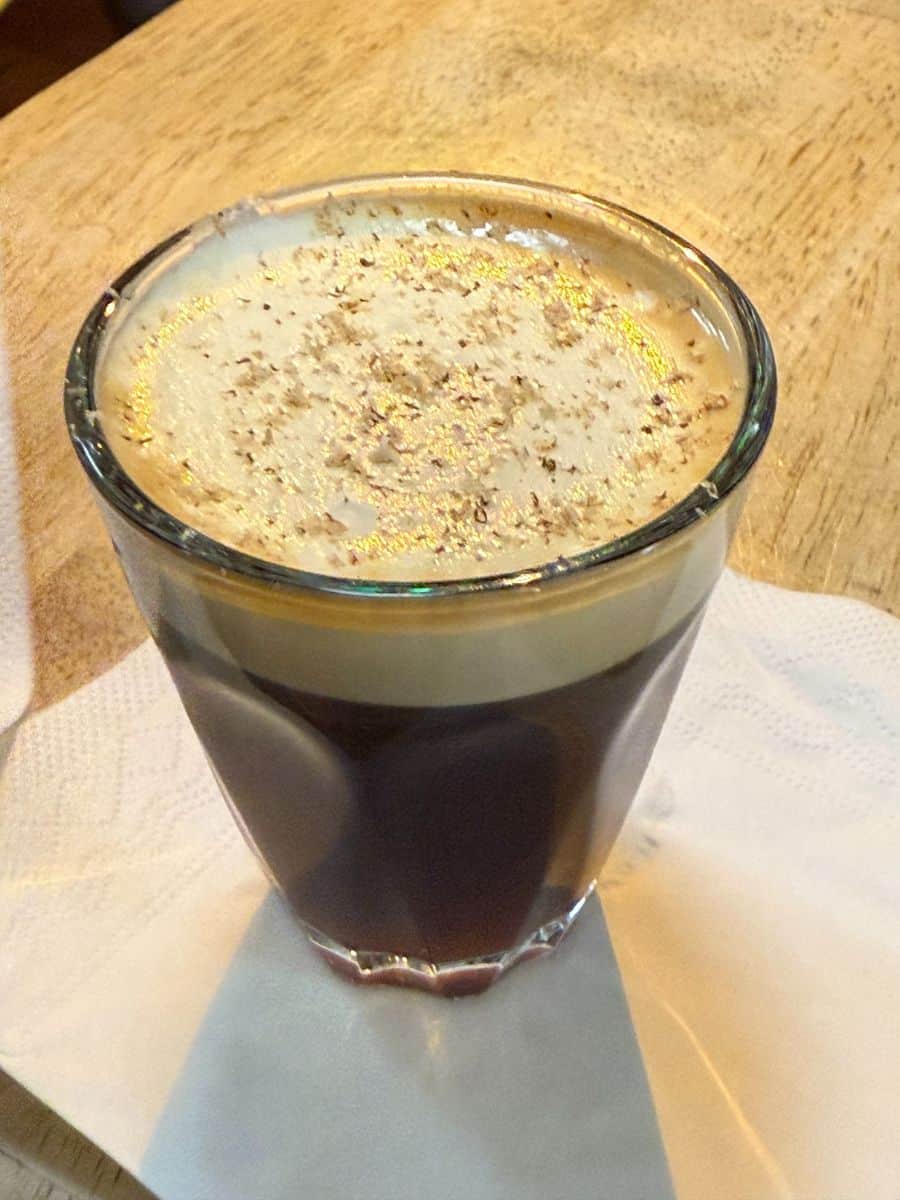 Glass of Irish coffee topped with whipped cream and grated nutmeg, served on a napkin in a cozy caf&eacute;.