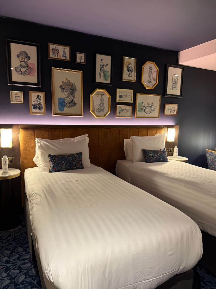 Twin beds in a Dublin boutique hotel, set against a dark wall decorated with vintage-style framed illustrations.