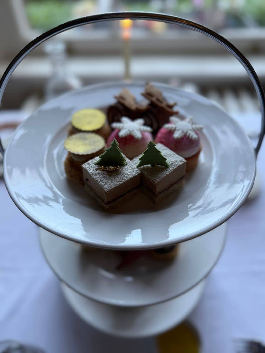 Tiered afternoon tea tray filled with festive pastries, including mini cakes topped with powdered sugar and chocolate decorations.