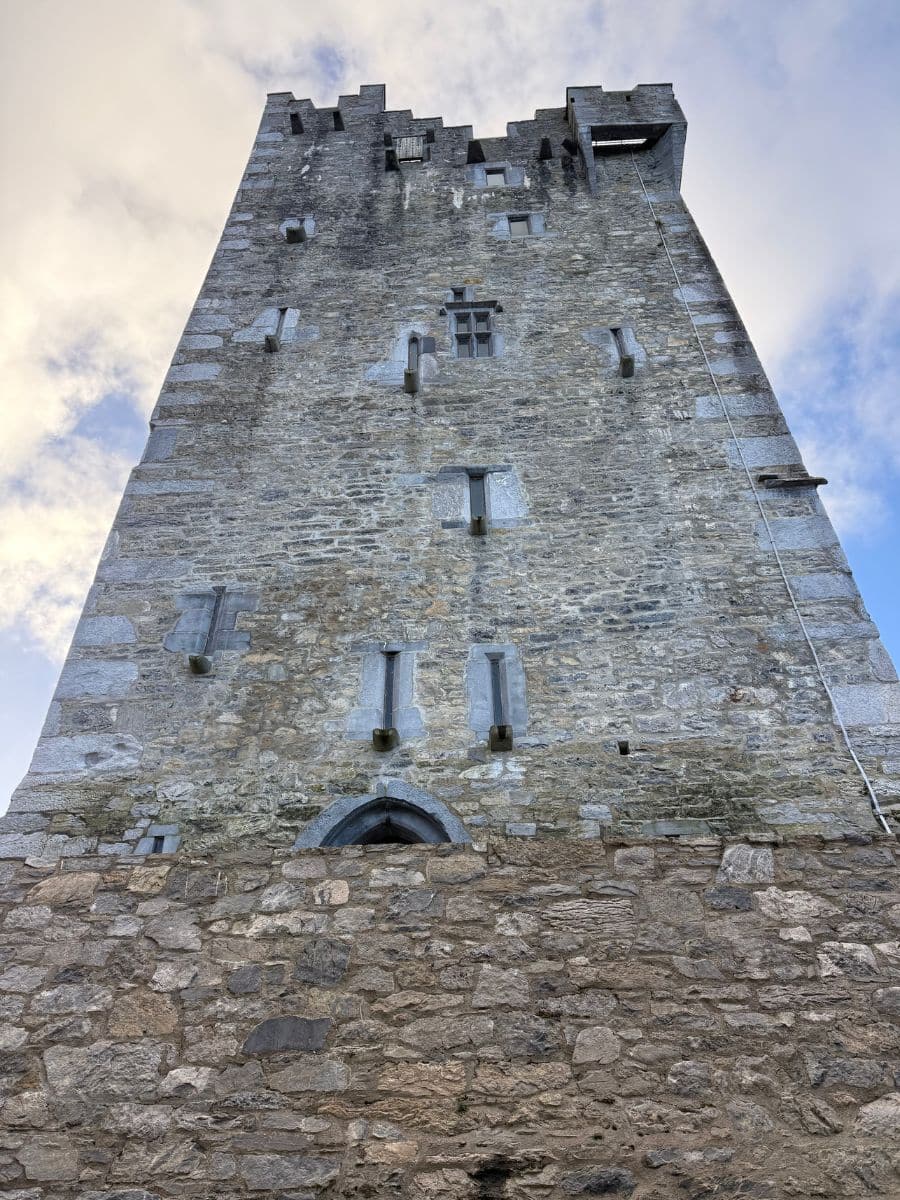 Upward view of the stone tower at Ross Castle, highlighting its medieval architecture against a cloudy sky.