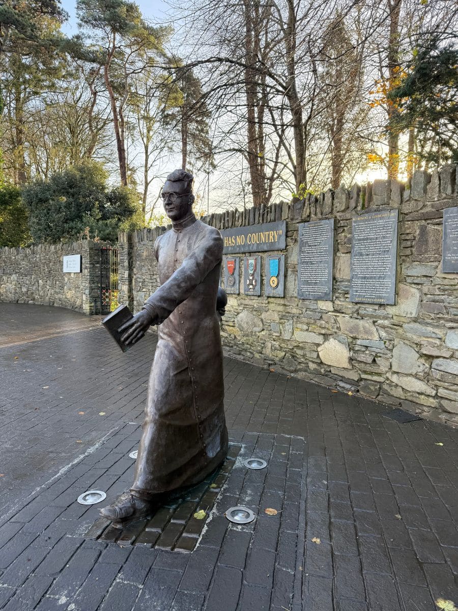 Bronze statue of Monsignor Hugh O’Flaherty at Killarney National Park, standing in front of a stone wall with memorial plaques.