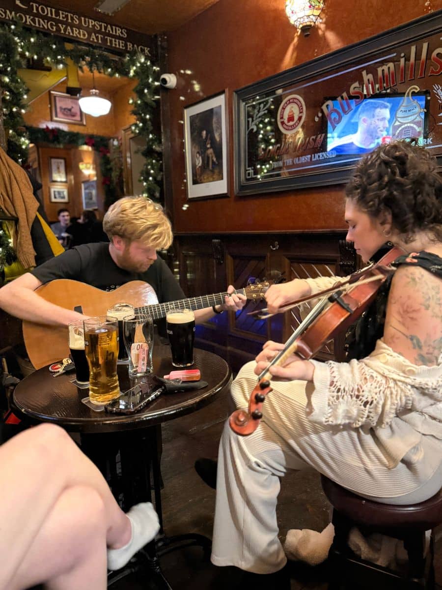 Two musicians playing guitar and fiddle inside a cozy Irish pub during an evening of traditional music.
