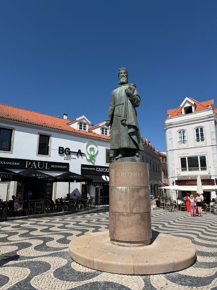 Statue of King Dom Pedro I in Cascais town center, surrounded by cafés, tiled pavement, and historic buildings