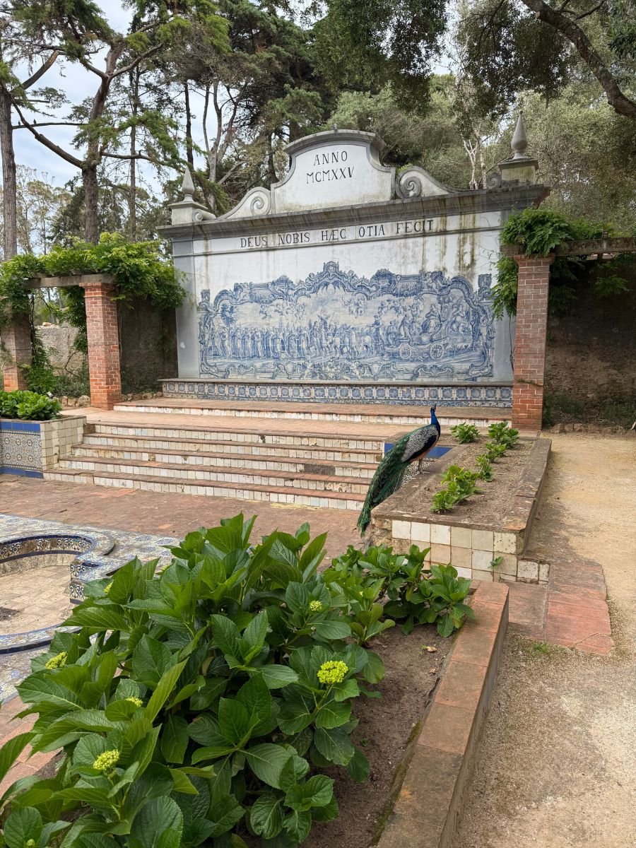 Historic azulejo tile panel in a garden in Cascais, Portugal, with a peacock standing near stone steps and greenery