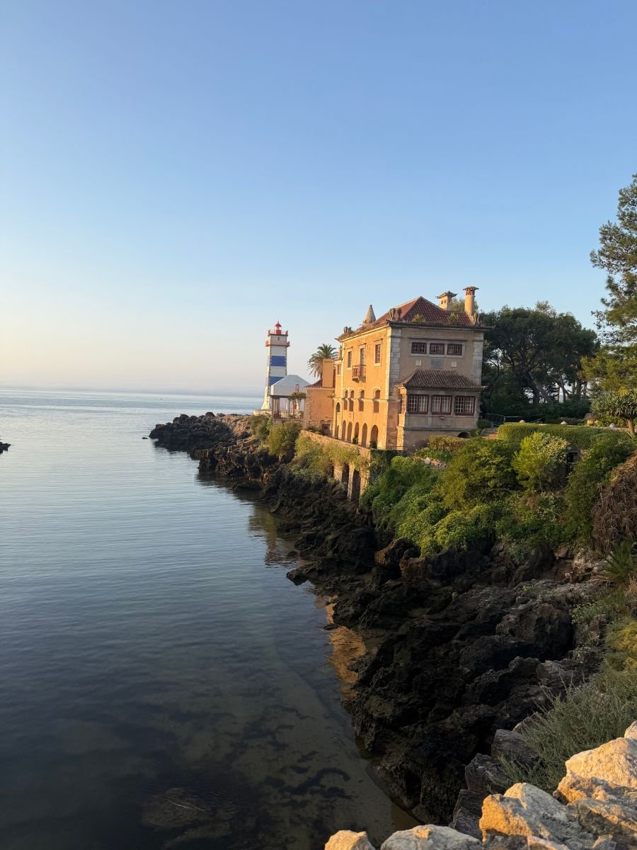 Cliffside view of Santa Marta Lighthouse and coastal buildings in Cascais, Portugal, overlooking calm ocean waters at sunset