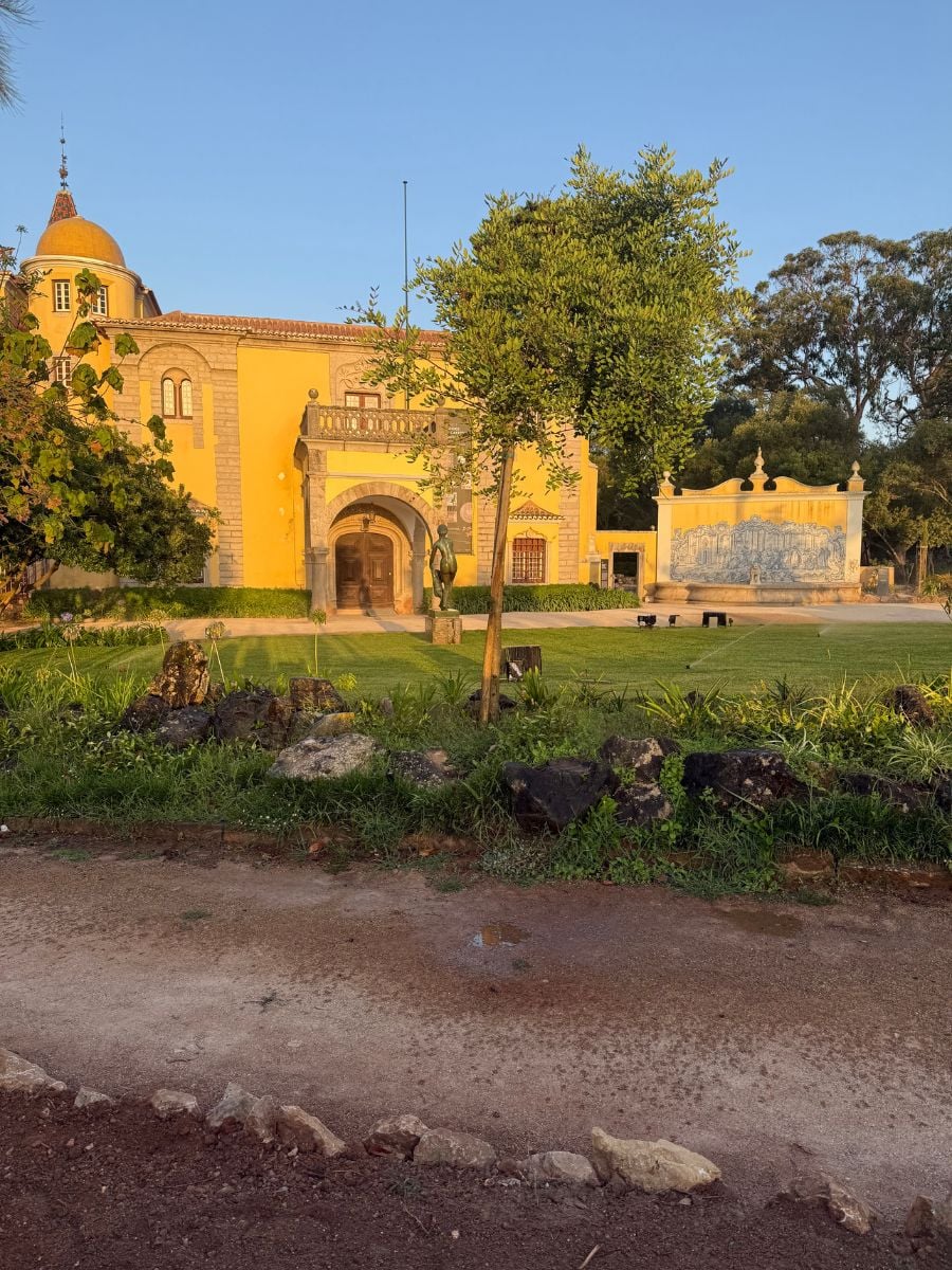 Yellow historic building and gardens in Cascais, Portugal, with manicured lawns, stone paths, and azulejo tile panels