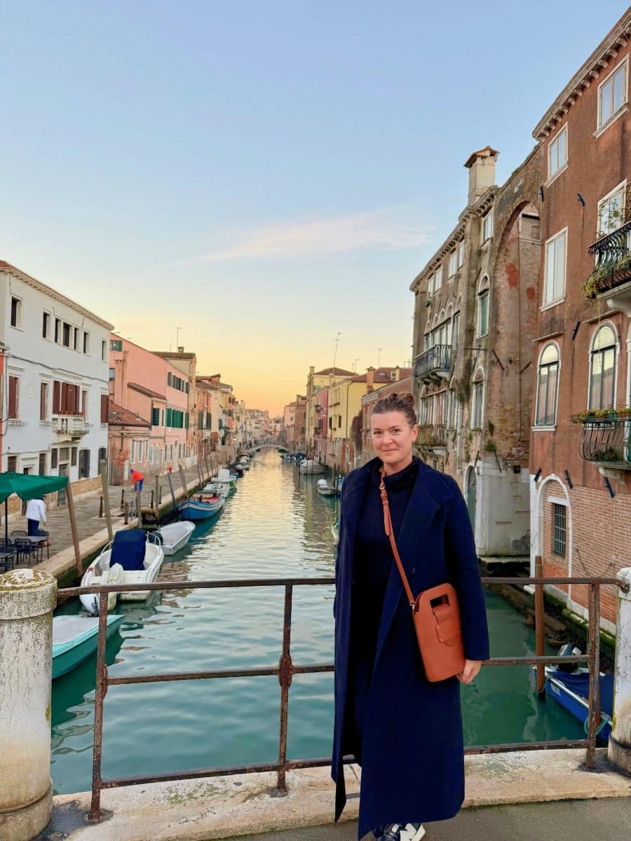 Woman standing on a bridge overlooking a canal at sunset in Venice.