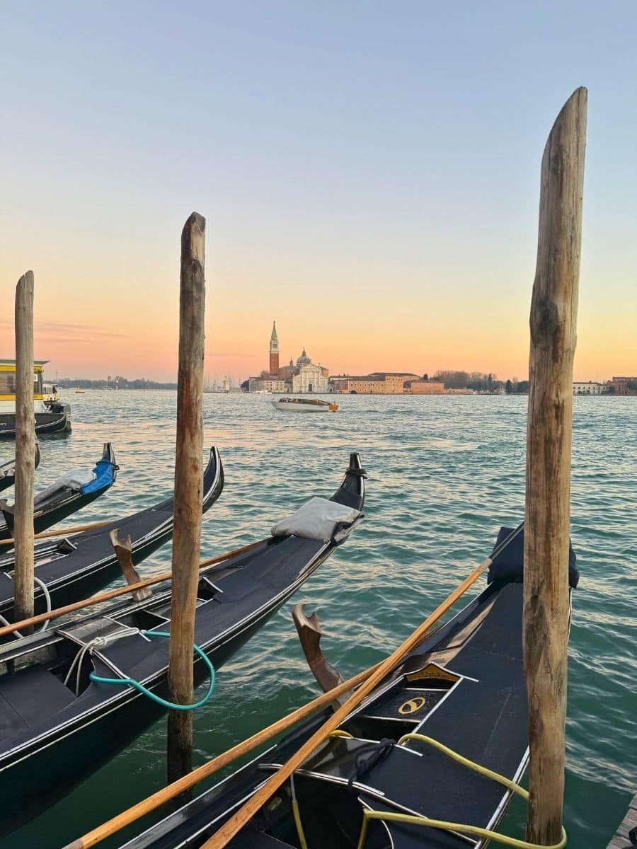 Gondolas moored on the Venetian lagoon with San Giorgio Maggiore visible at sunset.