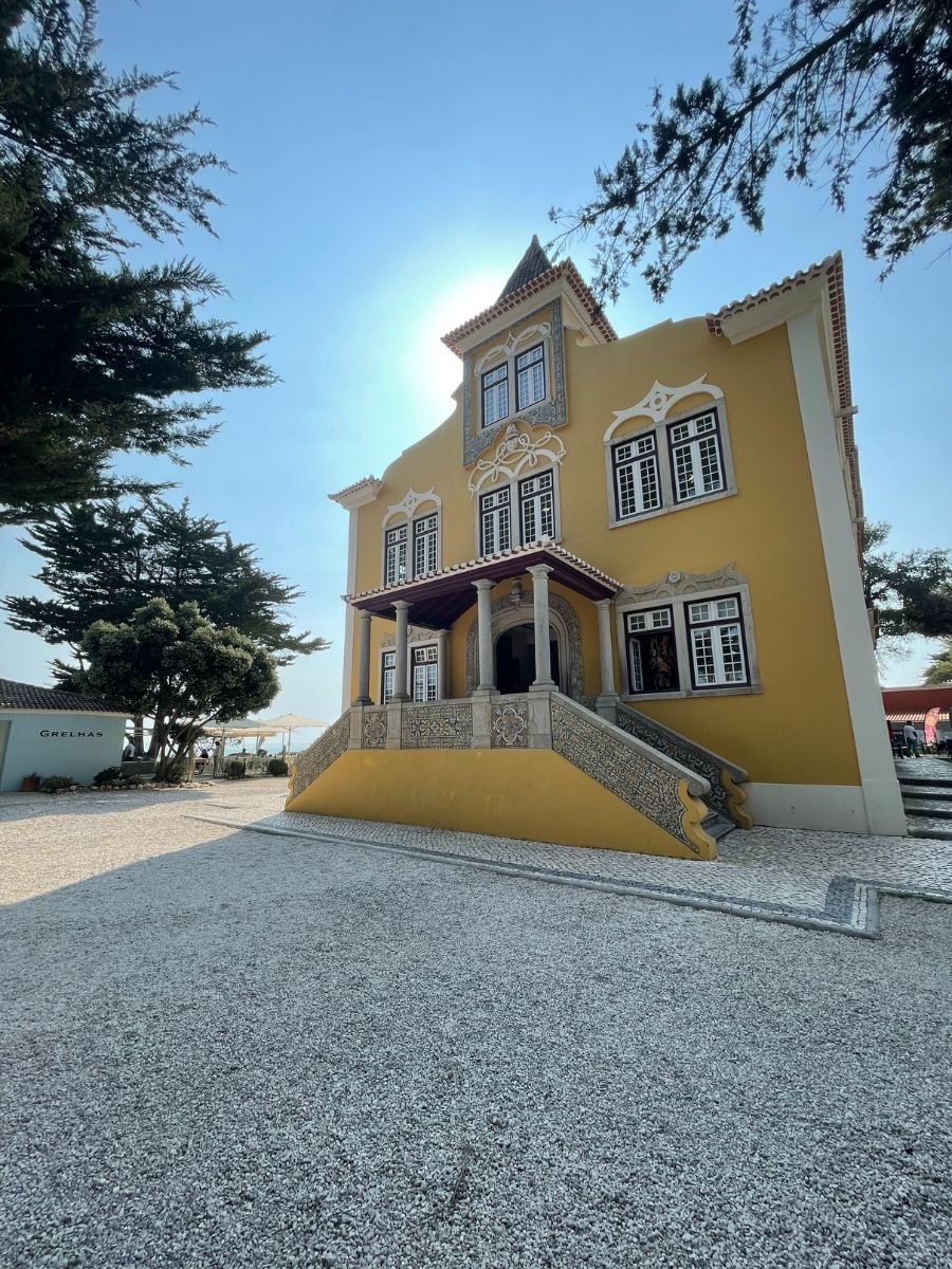 Yellow historic building in Cascais, Portugal, with decorative details, tiled steps, and a gravel courtyard surrounded by trees