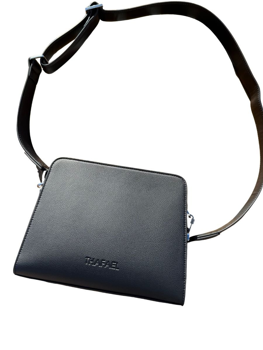 Black leather crossbody bag with adjustable strap resting on a wooden outdoor chair in sunlight.