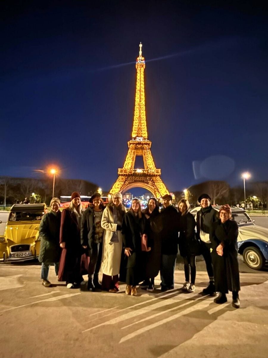 Group of women posing in front of the illuminated Eiffel Tower at night in Paris during a winter girls&rsquo; trip