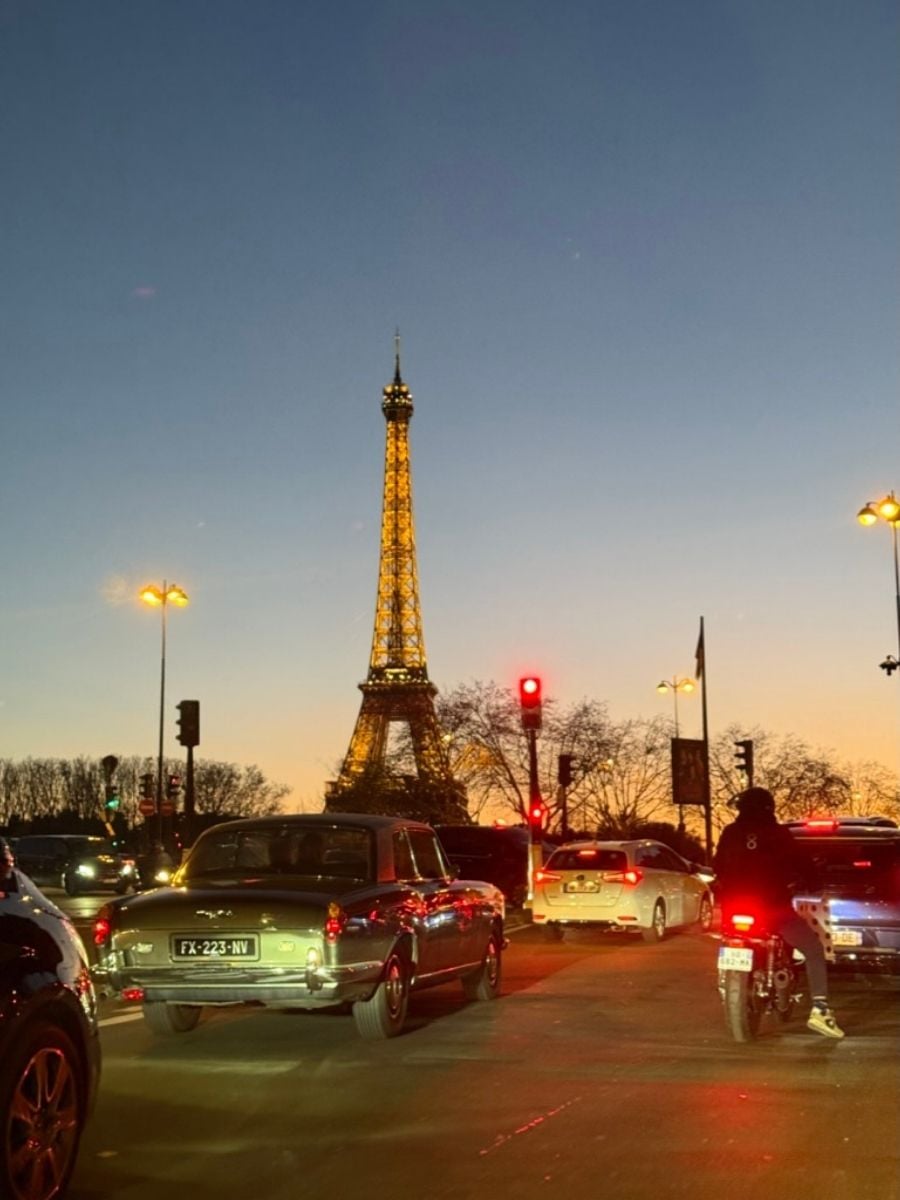 Evening traffic scene in Paris with the Eiffel Tower glowing at sunset and vintage cars on the street