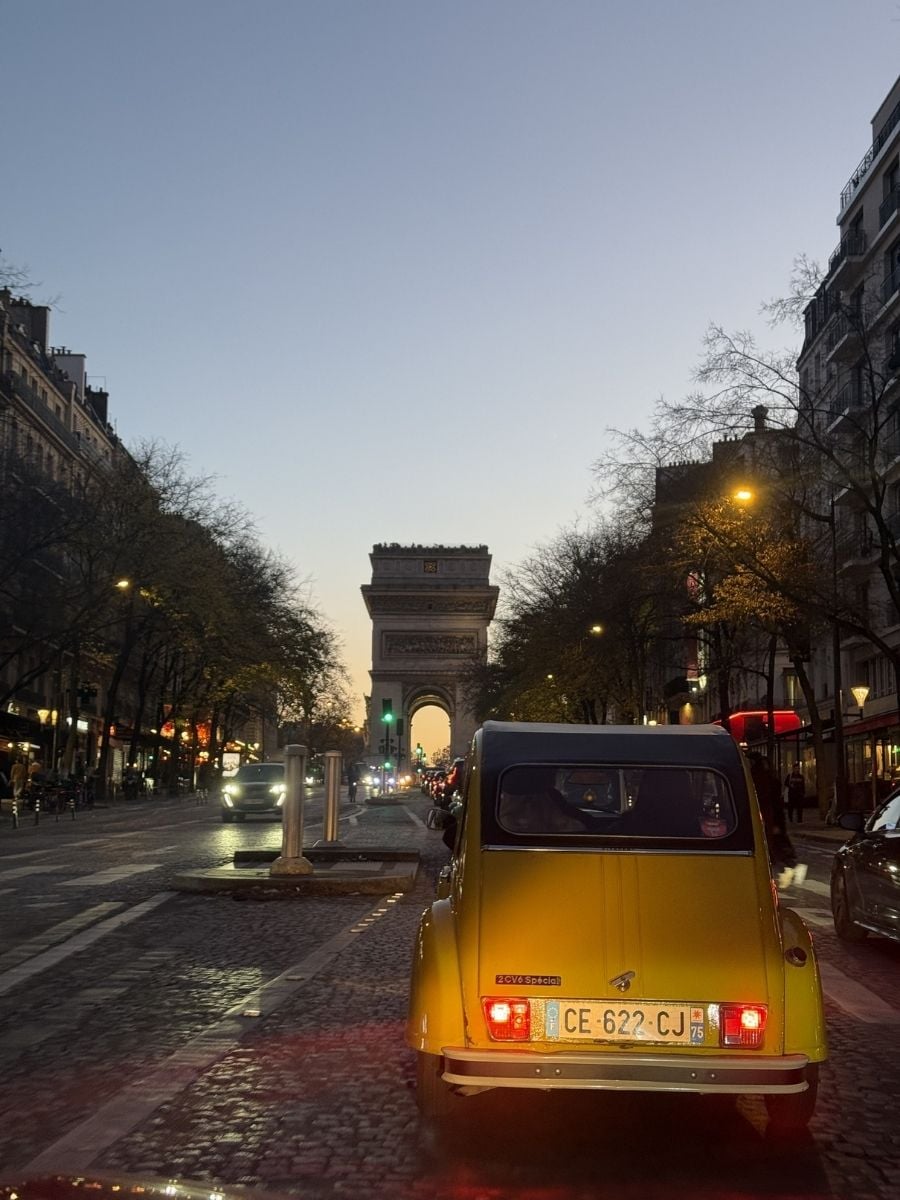 Yellow vintage car parked on Champs-&Eacute;lys&eacute;es facing Arc de Triomphe at dusk in Paris