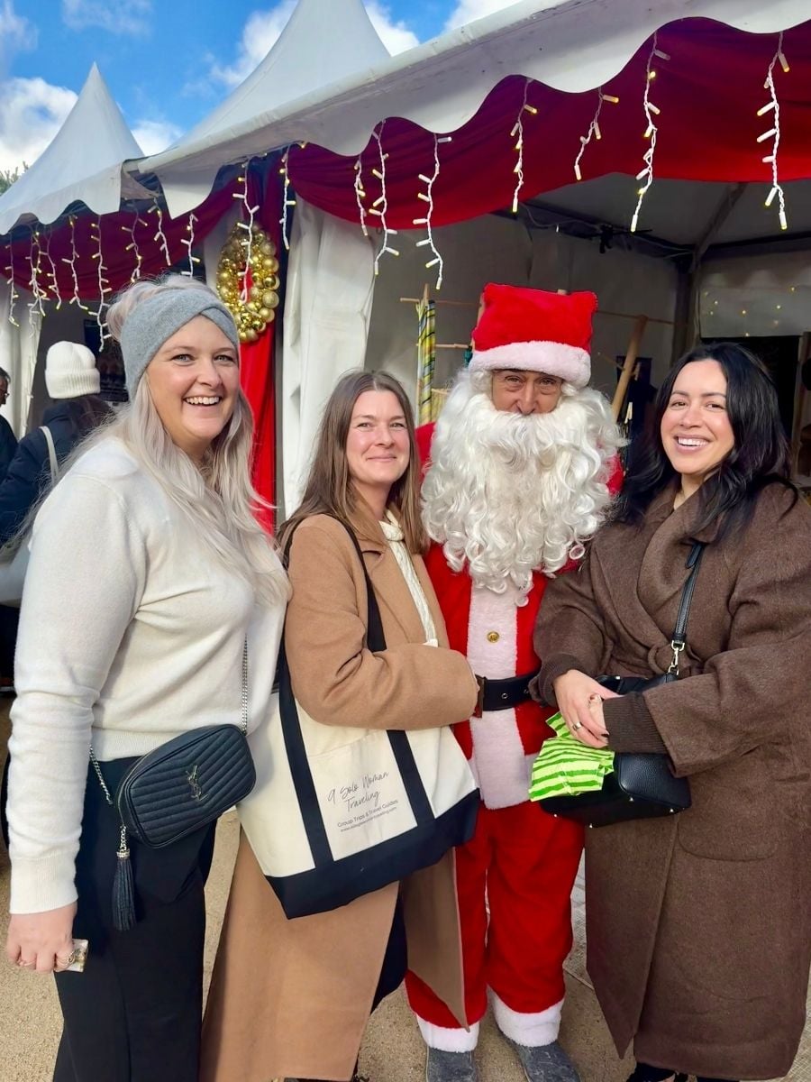 Group of women posing with Santa Claus at a Christmas market in Paris, France, during a festive winter trip.