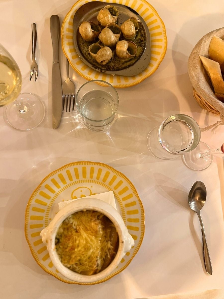 Traditional French dinner table with escargot, onion soup, bread, and wine at a restaurant in Paris.