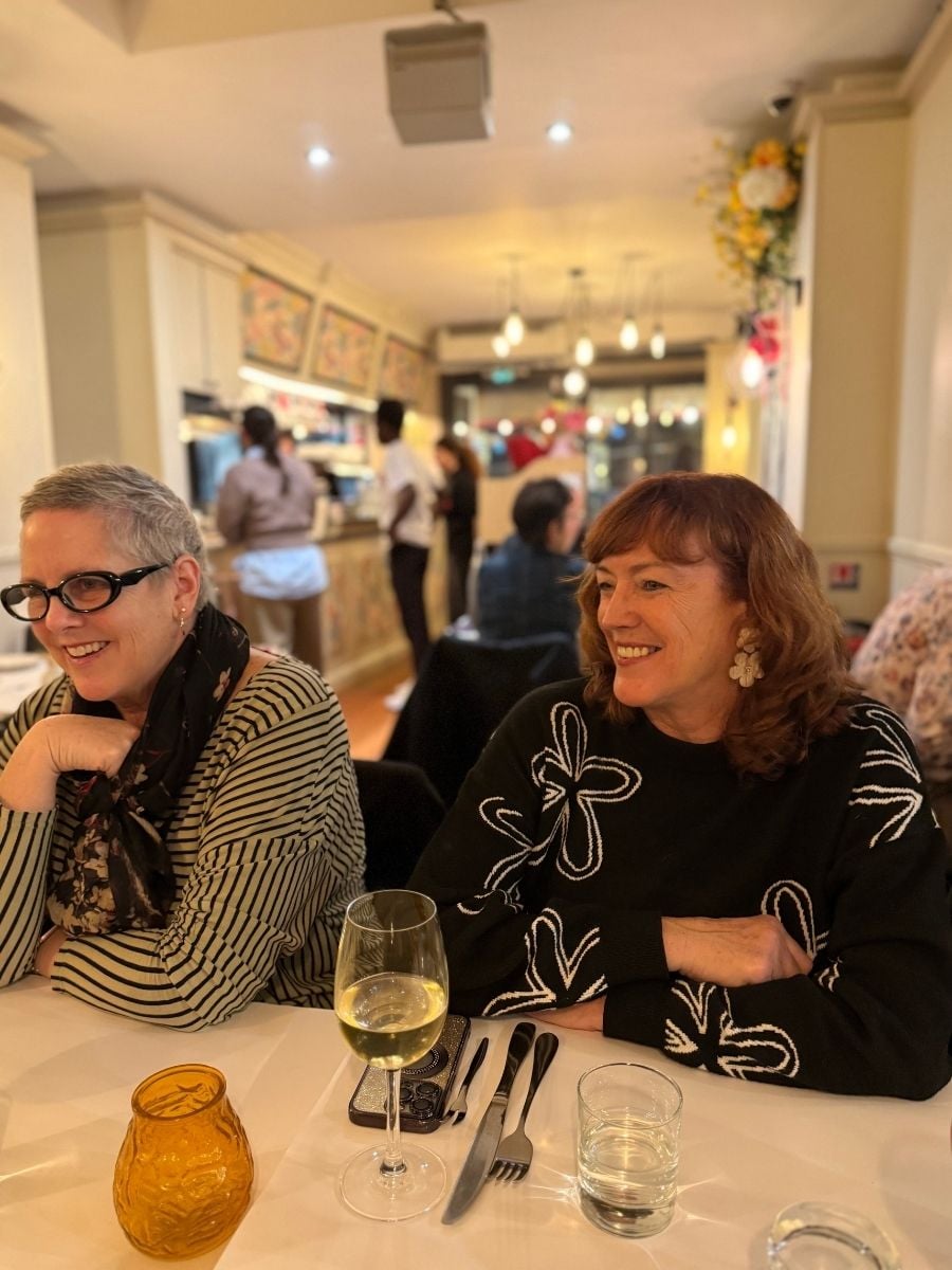Two women laughing over dinner and wine at a restaurant in Paris during a group trip.