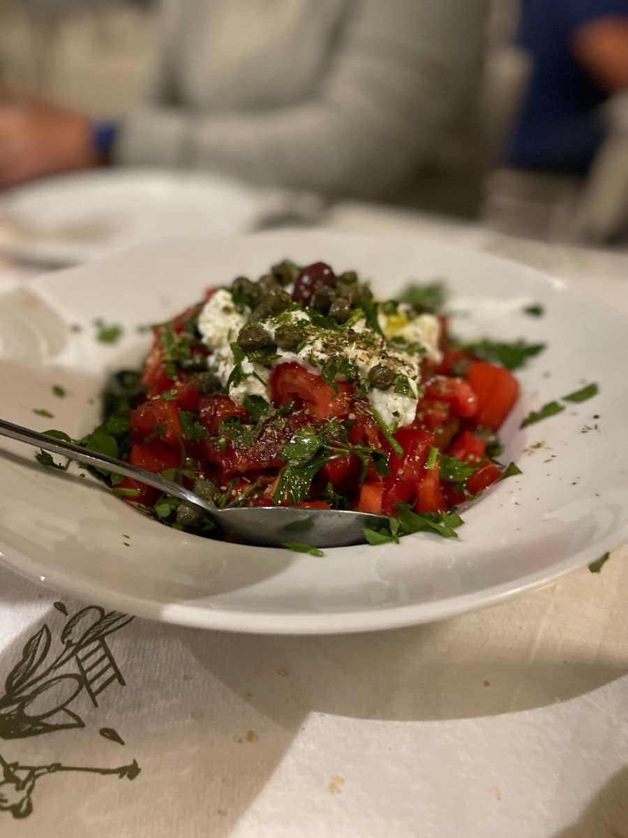 Fresh tomato and feta salad topped with herbs and capers served at a local taverna on an Athens food tour.