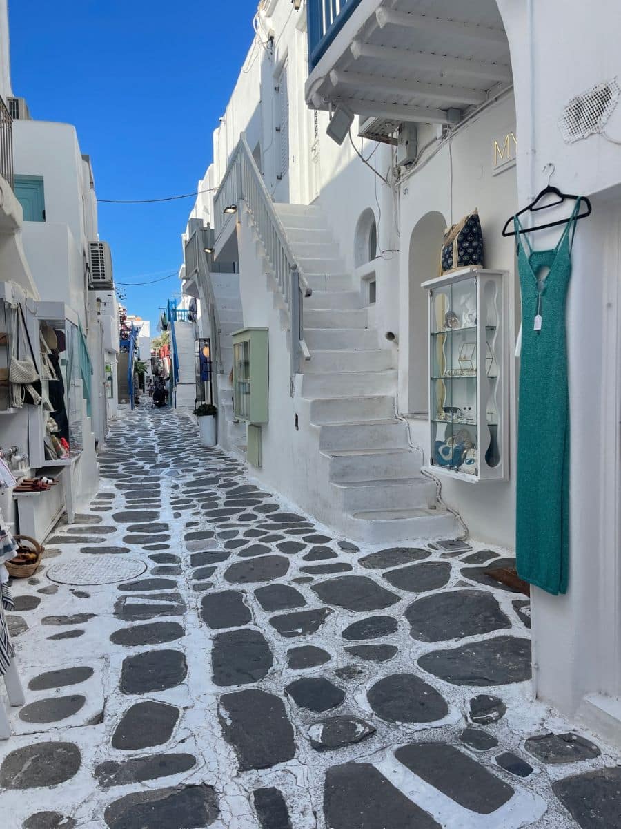 Narrow white alley with stone path and boutique shops in Mykonos Town