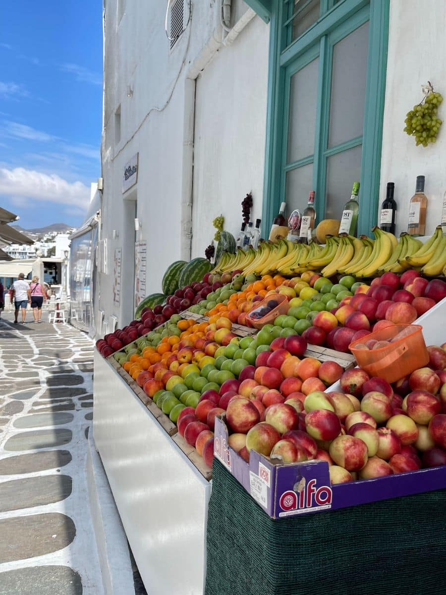 Fresh fruit stand with bananas, peaches, and apples along a stone street in Mykonos Town