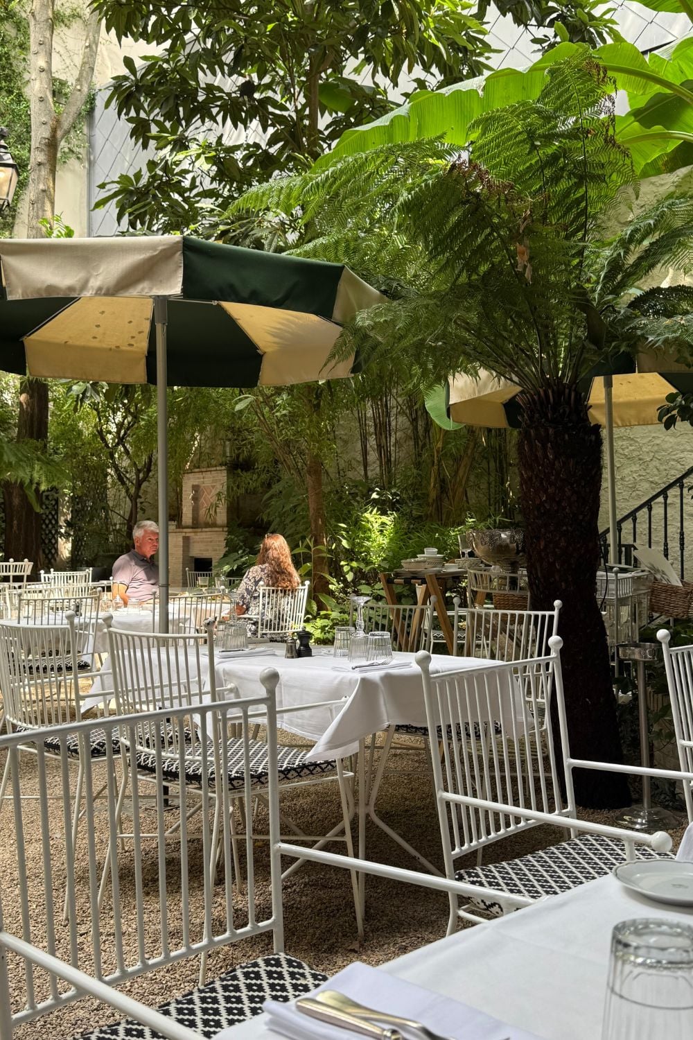 Outdoor garden courtyard at H&ocirc;tel Eldorado Paris with white tables, umbrellas, and lush greenery creating a peaceful dining setting