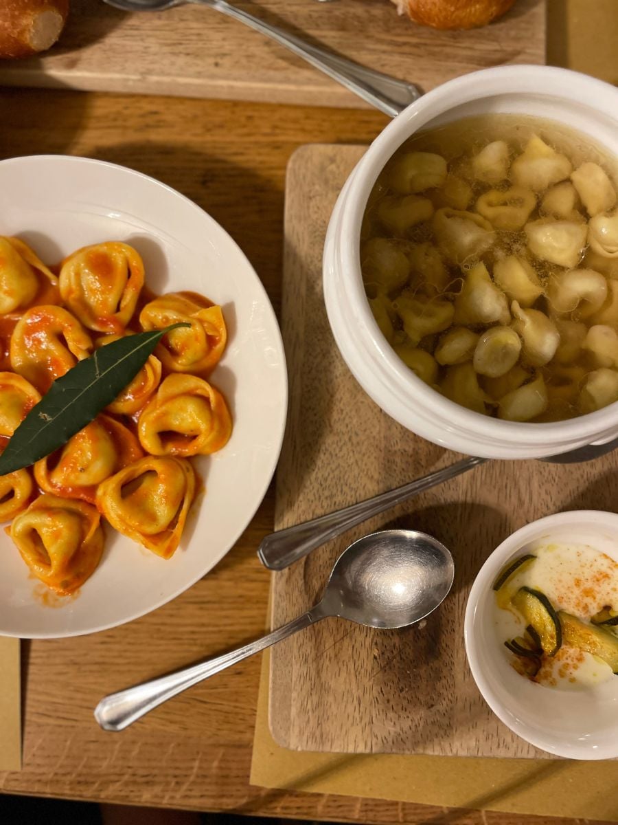 Traditional Bologna meal with tortellini in broth, tortellini with tomato sauce, and creamy baked zucchini on a wooden table