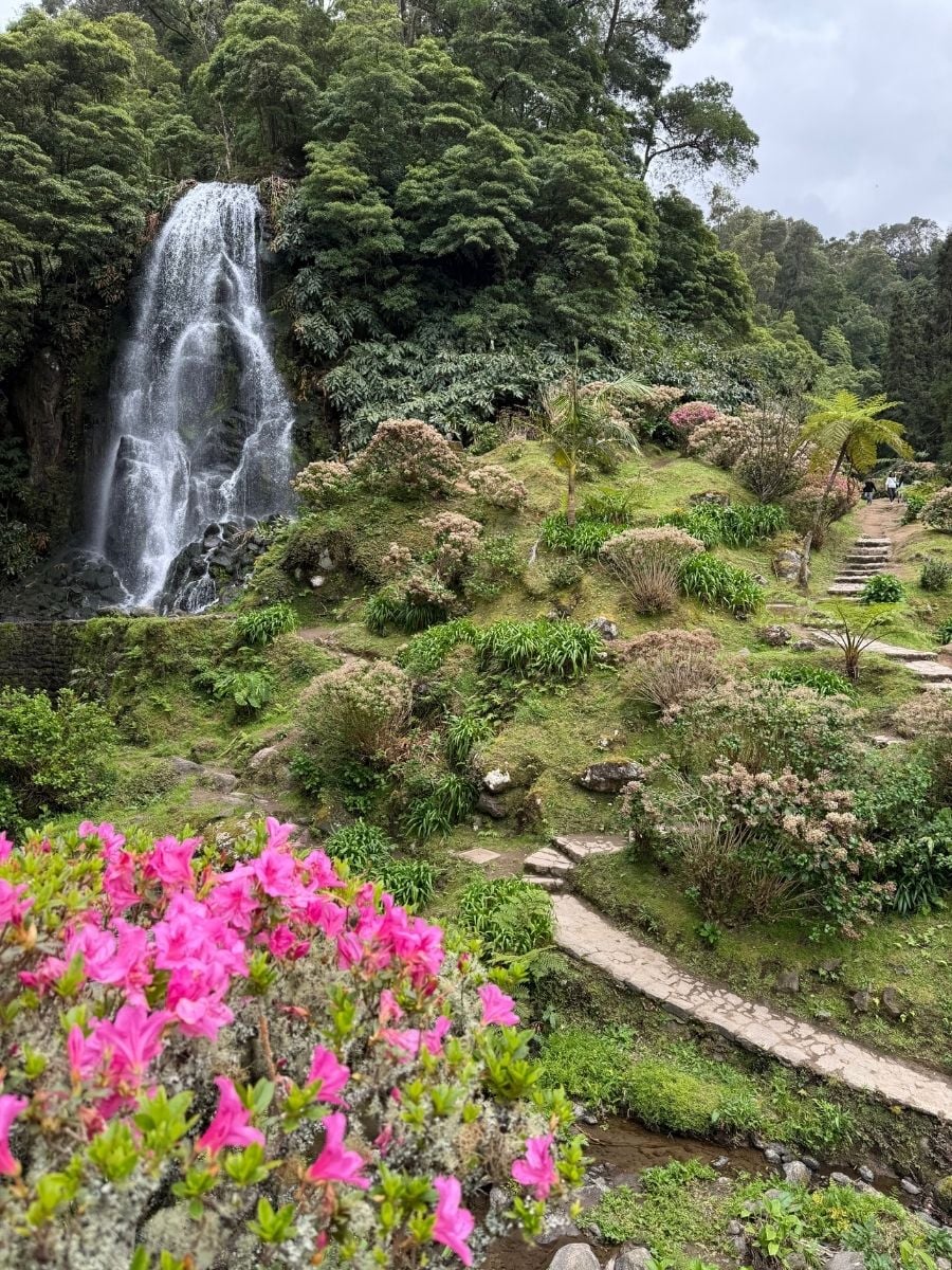 Close view of waterfall and garden paths in S&atilde;o Miguel, Azores with vibrant greenery, stone steps, and pink flowers in bloom