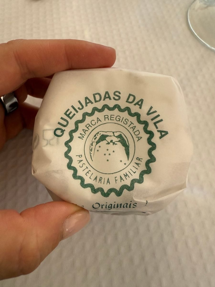 Traditional Queijadas da Vila pastry wrapped in paper in S&atilde;o Miguel, Azores held by hand, highlighting a local sweet specialty