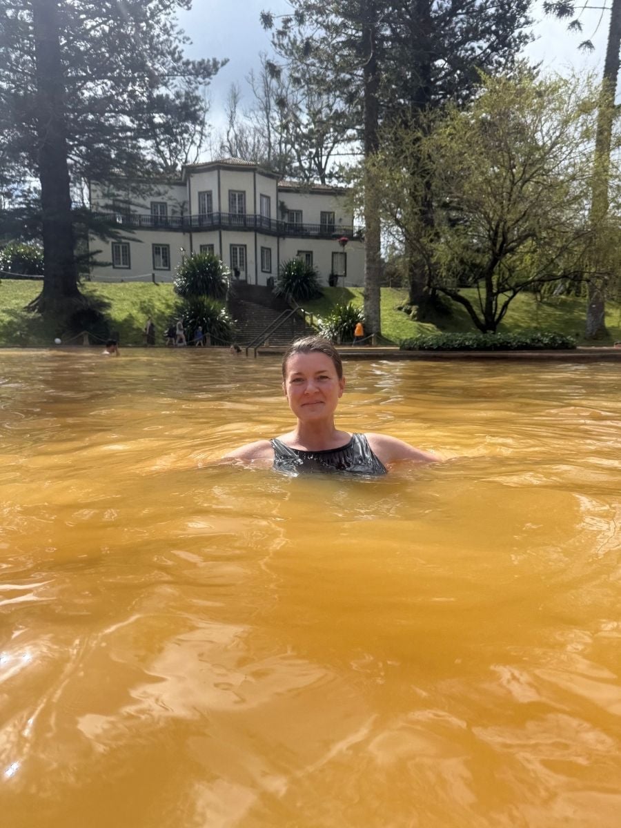 Melissa bathing in the famous orange thermal pool at Parque Terra Nostra, Furnas, S&atilde;o Miguel, Azores with historic building in the background