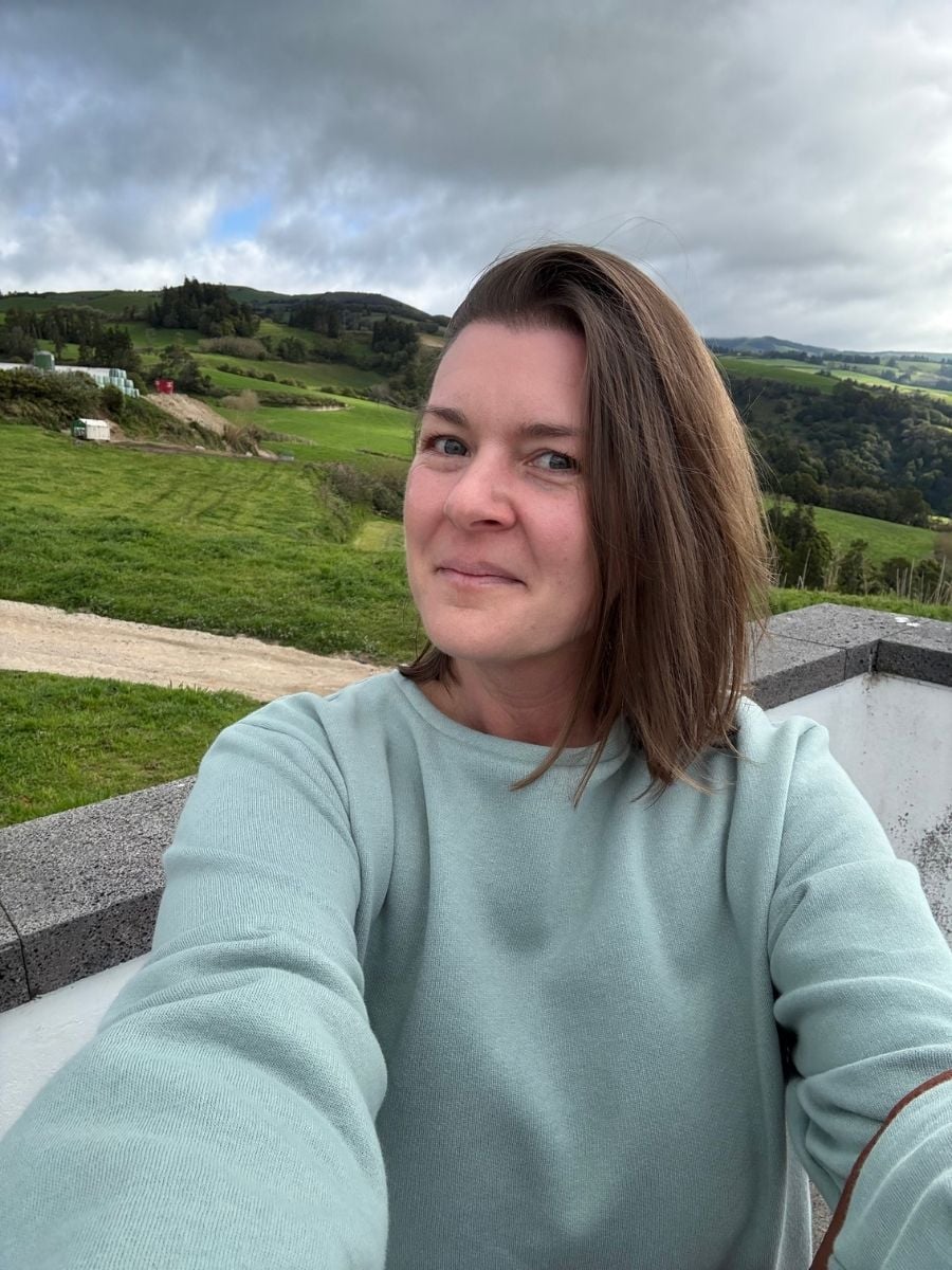Melissa taking a selfie overlooking lush rolling hills in S&atilde;o Miguel, Azores with patchwork fields and cloudy sky in the background