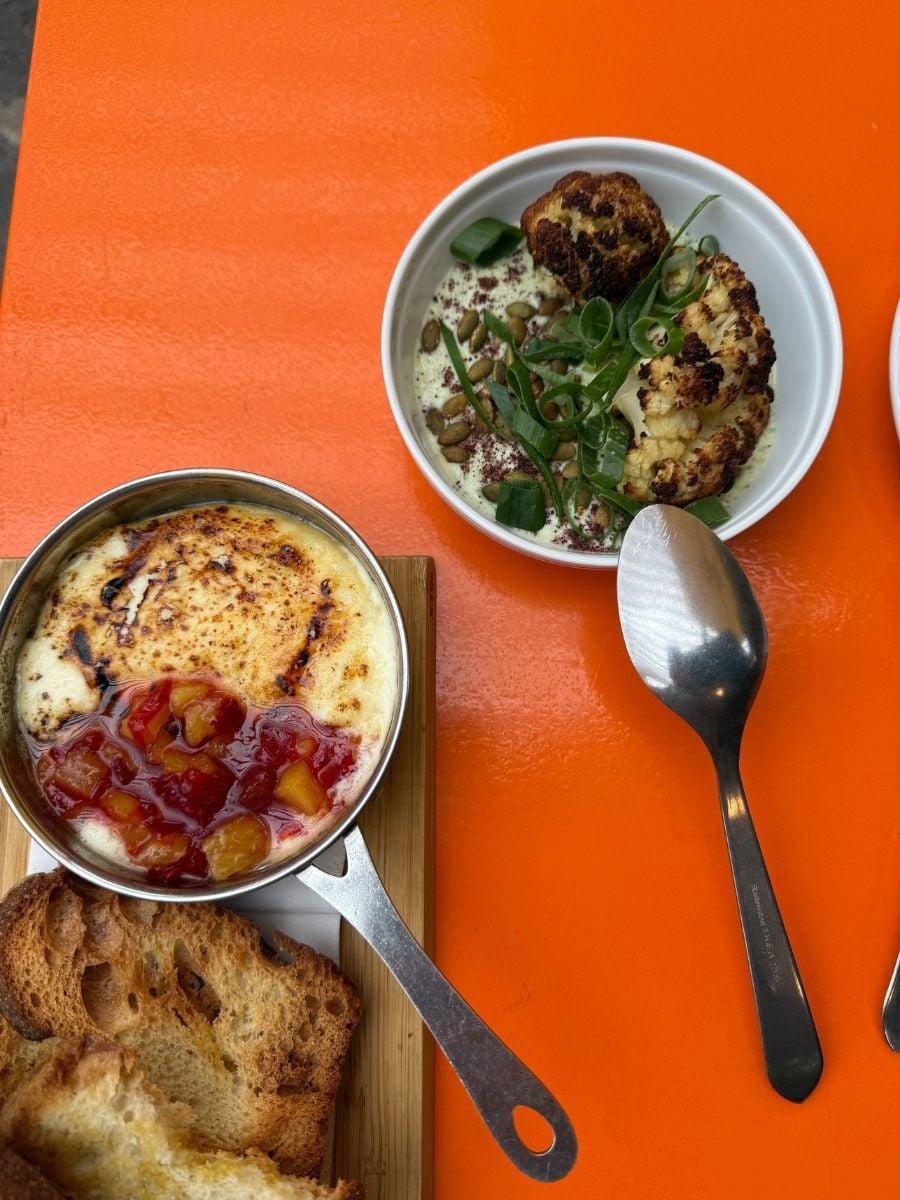 Baked cheese dish with fruit topping and roasted cauliflower served on an orange table in S&atilde;o Miguel, Azores restaurant setting