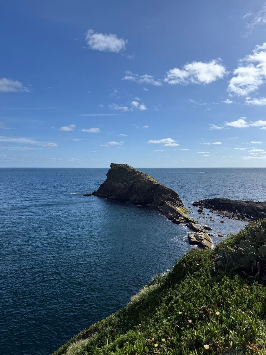 Rocky islet rising from the Atlantic Ocean in S&atilde;o Miguel, Azores viewed from a coastal cliff with lush greenery and clear blue skies