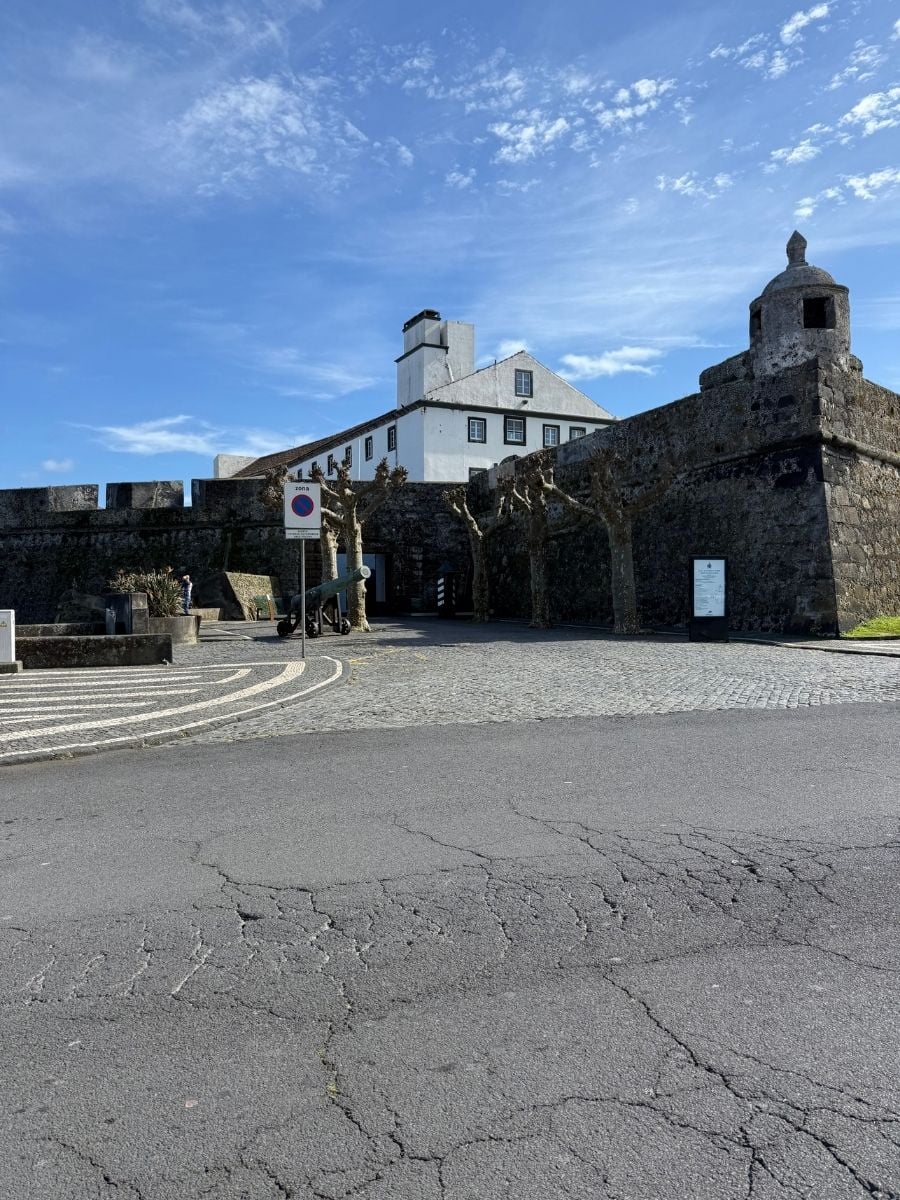 Historic stone fort with cannons and white building in S&atilde;o Miguel, Azores set along a cobblestone square under a bright blue sky