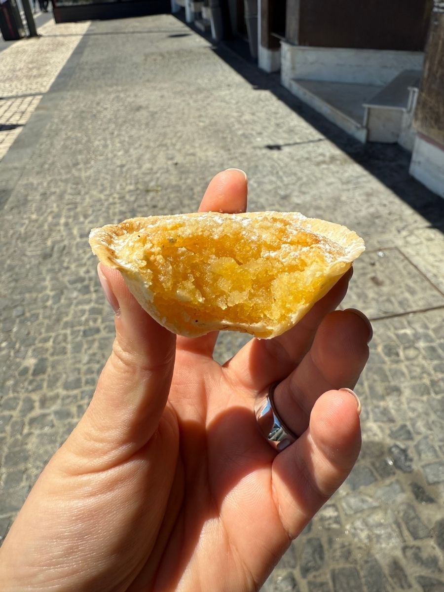Partially eaten custard tart held by hand on a cobblestone street in S&atilde;o Miguel, Azores showing its flaky crust and sweet filling