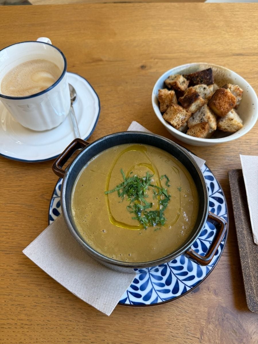 Creamy vegetable soup topped with herbs and olive oil served with croutons and coffee in S&atilde;o Miguel, Azores on a wooden table