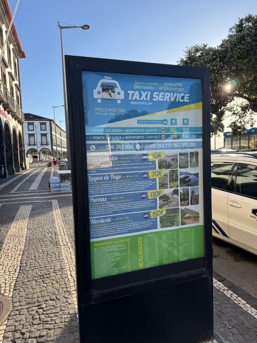 Taxi service sign on a cobblestone street in Ponta Delgada, S&atilde;o Miguel, Azores with pricing details and parked cars nearby