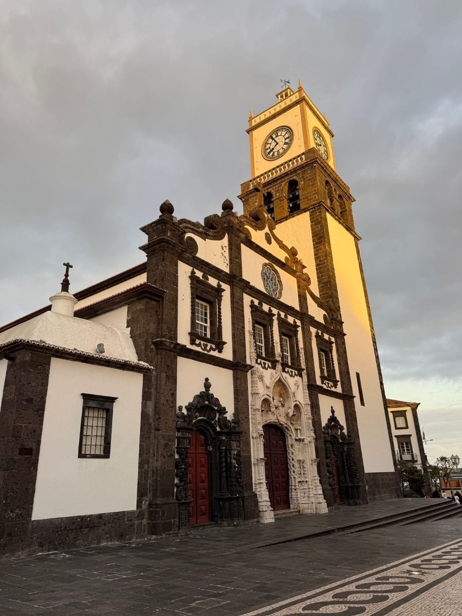 Historic church with a clock tower glowing in warm light in Ponta Delgada, S&atilde;o Miguel, Azores under a cloudy evening sky