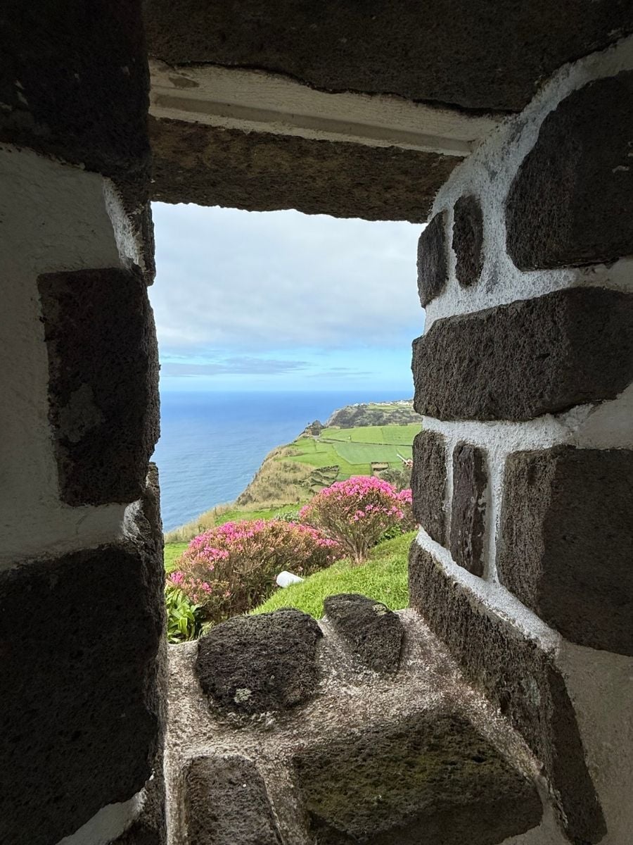 View through a stone window toward coastal cliffs and pink flowers in S&atilde;o Miguel, Azores with scenic ocean vistas