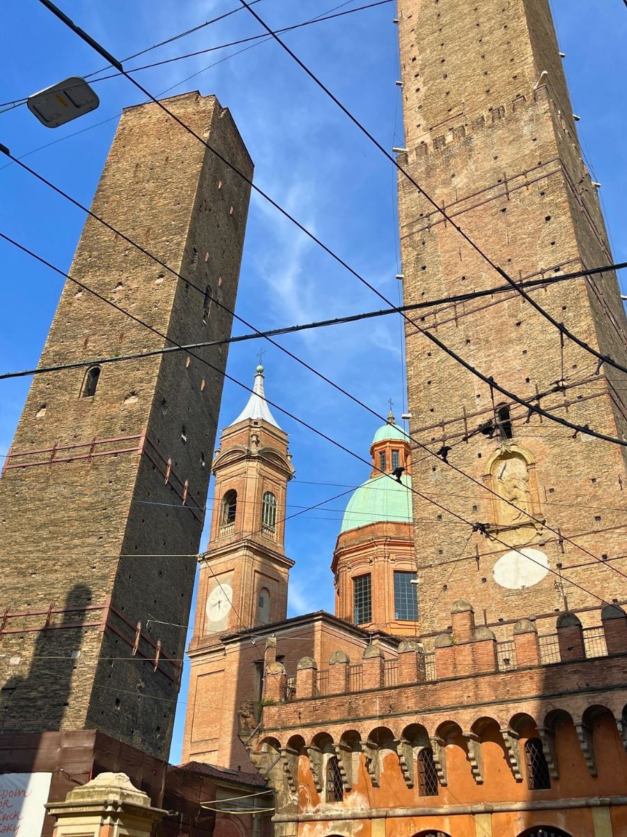 Medieval Two Towers in Bologna (Asinelli and Garisenda) rising above historic buildings and church domes under a blue sky