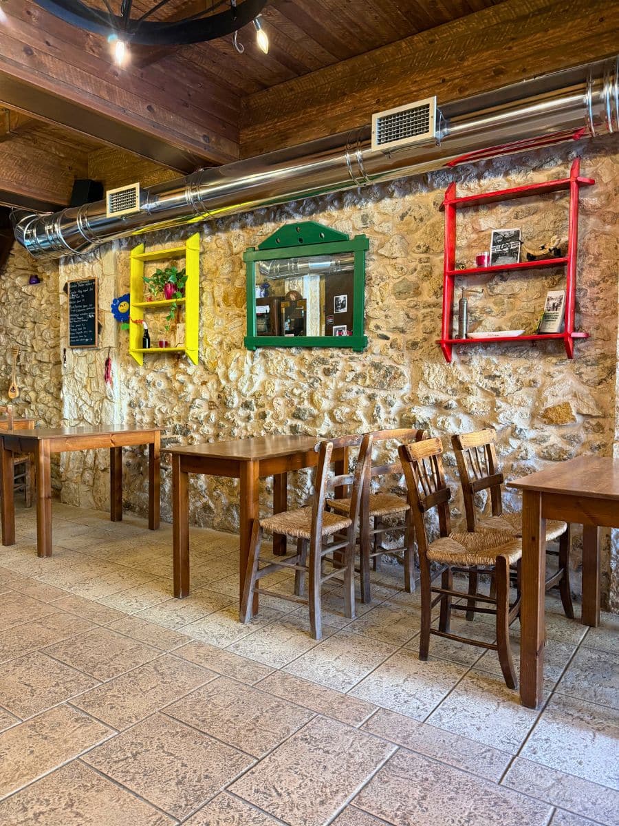 Traditional Cretan taverna interior with stone walls, wooden tables, and colorful rustic window decorations in Heraklion, Crete.
