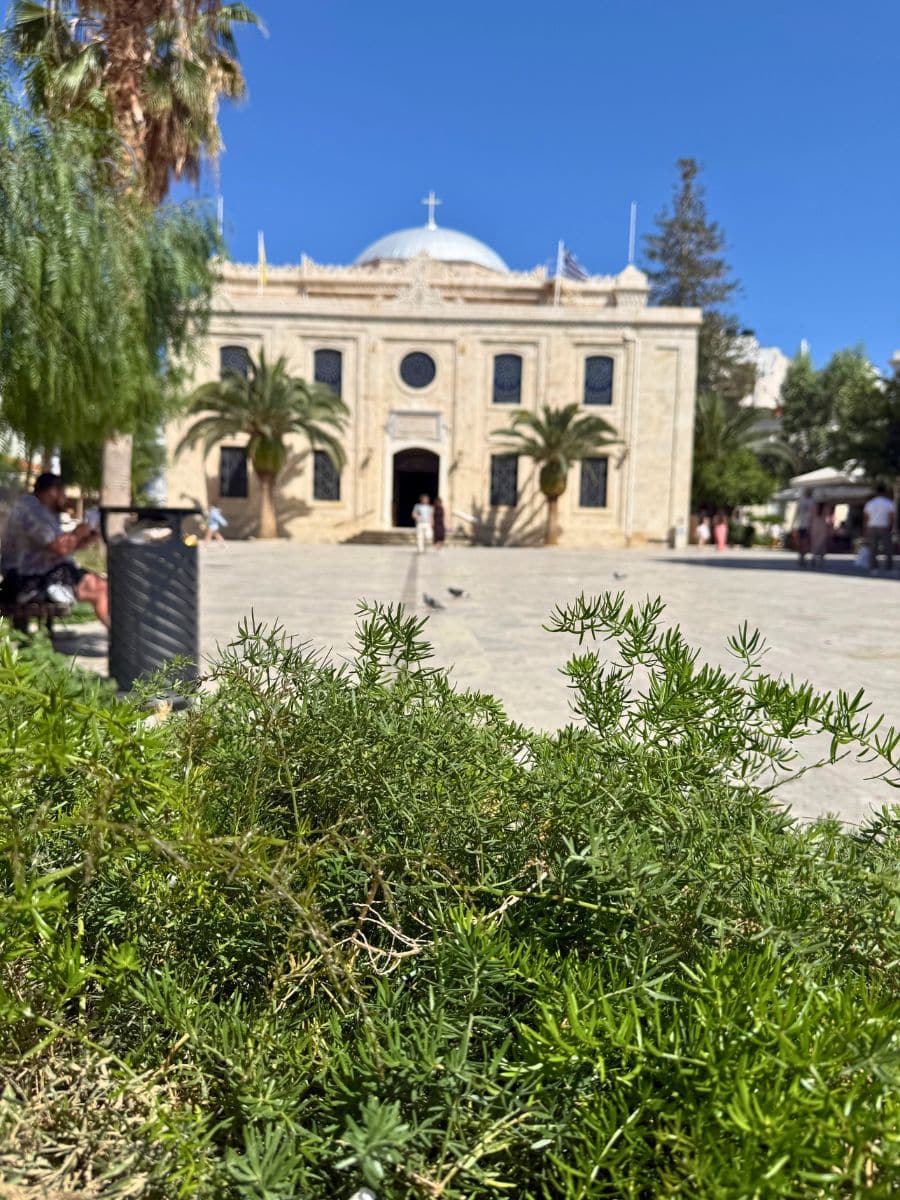 View of Saint Titus Church in Heraklion, Crete, with lush greenery in the foreground on a sunny day.