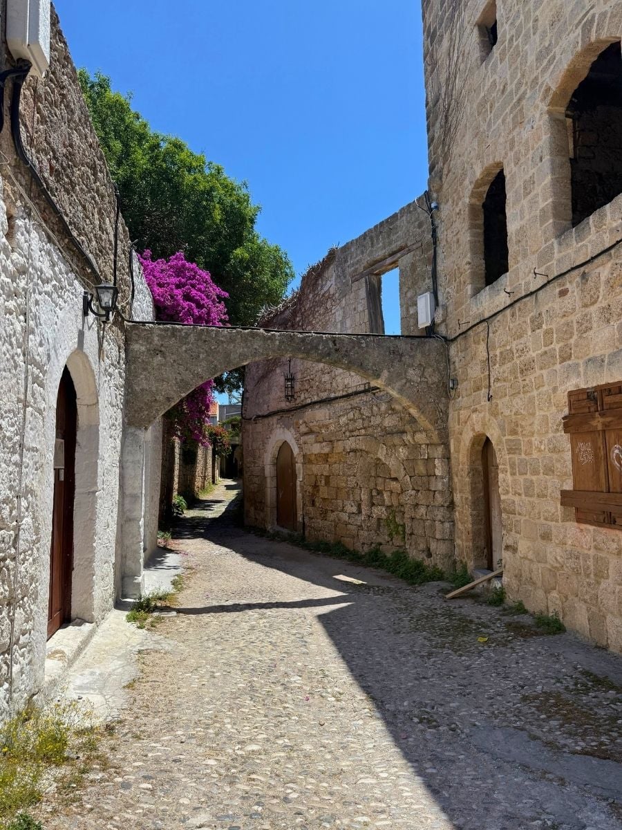 Quiet cobblestone alley with medieval stone buildings and a shaded archway in Rhodes Old Town, Rhodes, Greece.