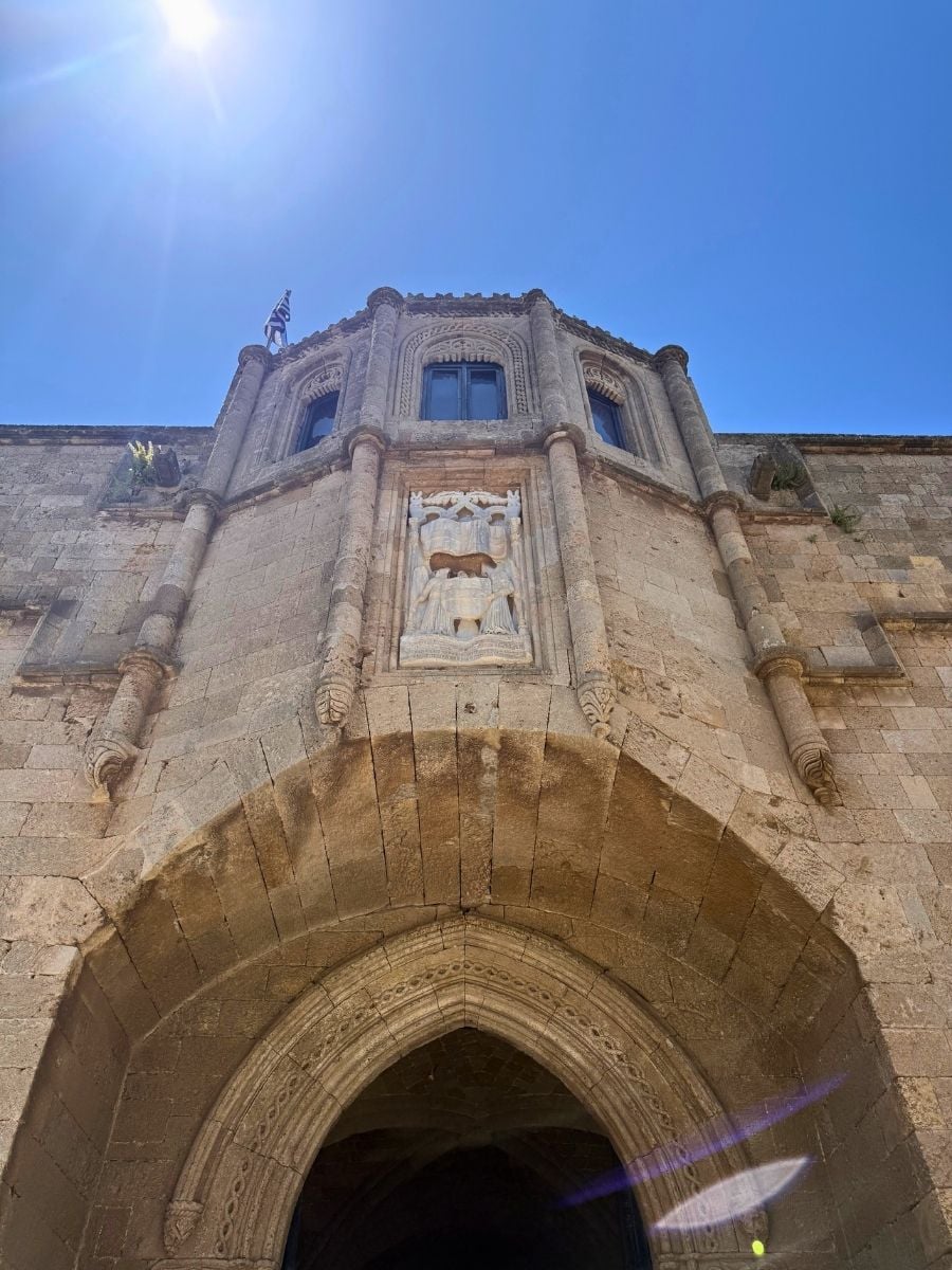 Ornate medieval gateway with carved stone details beneath a bright blue sky in Rhodes Old Town, Rhodes, Greece.