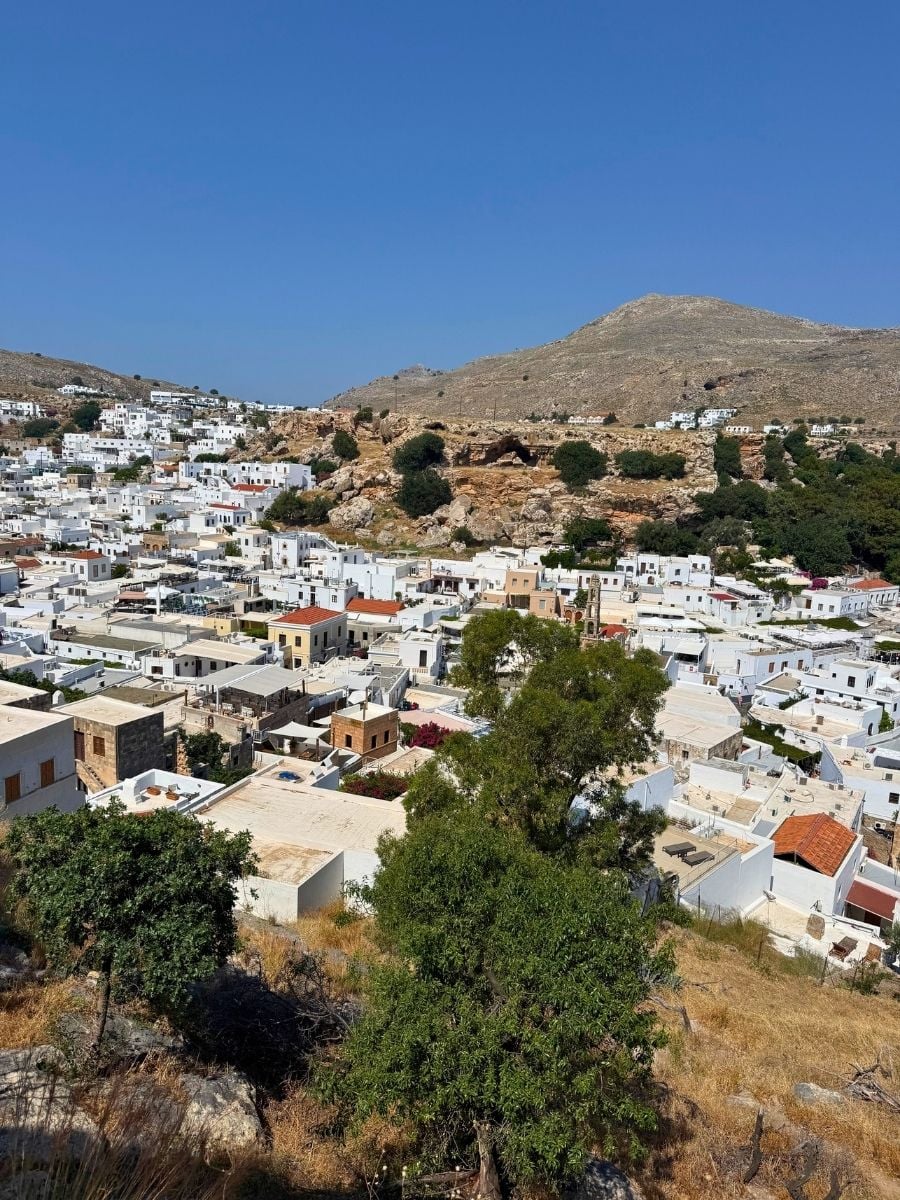 Panoramic view over the whitewashed village of Lindos, Rhodes, Greece with rocky hills and traditional architecture.