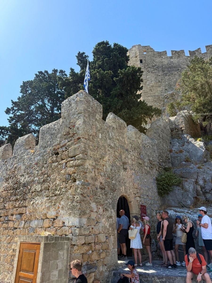 Ancient stone entrance to the Acropolis of Lindos in Rhodes, Greece with visitors exploring the medieval fortress.