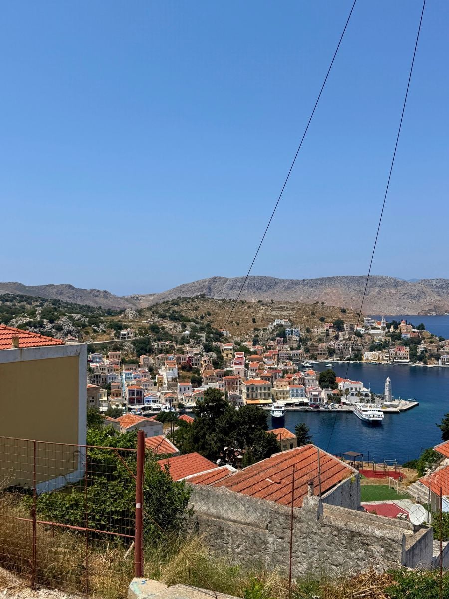 Panoramic view of Symi, Greece overlooking the picturesque harbor, pastel waterfront buildings, and rugged hills surrounding the bay.