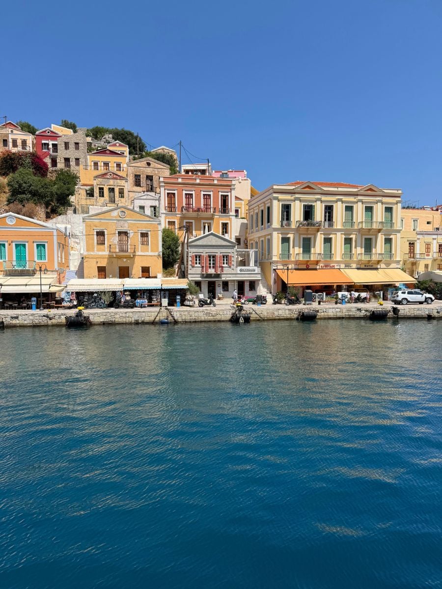 Vibrant waterfront architecture in Symi, Greece featuring pastel neoclassical buildings overlooking the sparkling Aegean harbor.