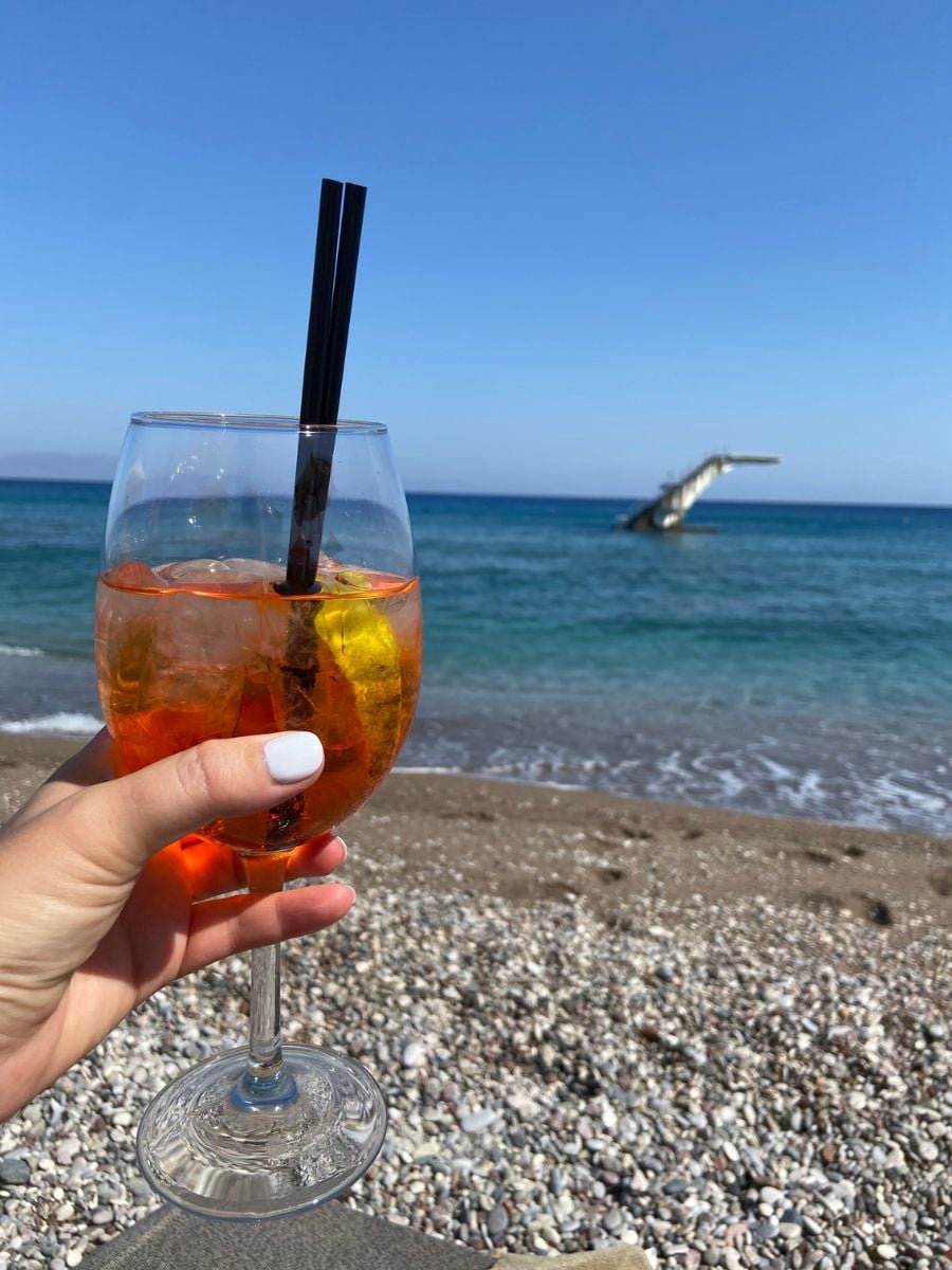 Woman holding an aperol spritz at the beach in Rhodes